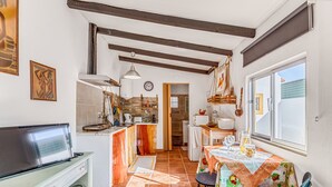 A kitchen with a TV, a dining table with chairs, a window, and a door leading to another room. - Holiday Home "O Mundo Da Lua - Galinheiro" with Shared Garden and Wi-Fi (São Simão)