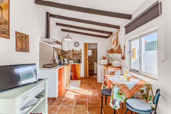 A kitchen with a TV, a dining table with chairs, a window, and a door leading to another room.