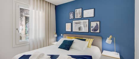 A neatly made bed with towels, a bedside lamp, and artwork on the wall.