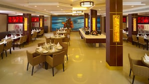 A spacious restaurant with multiple dining tables and chairs, a central decorative wall with a ship painting, and a modern ceiling design. - AAR Royal Residency - Palmyra (Palayankottai)