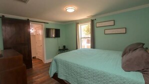 A bedroom with a bed, a television, a door, and a window.
