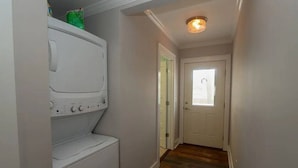 A laundry room with a washer and dryer, a wooden floor, and a door leading to another room.