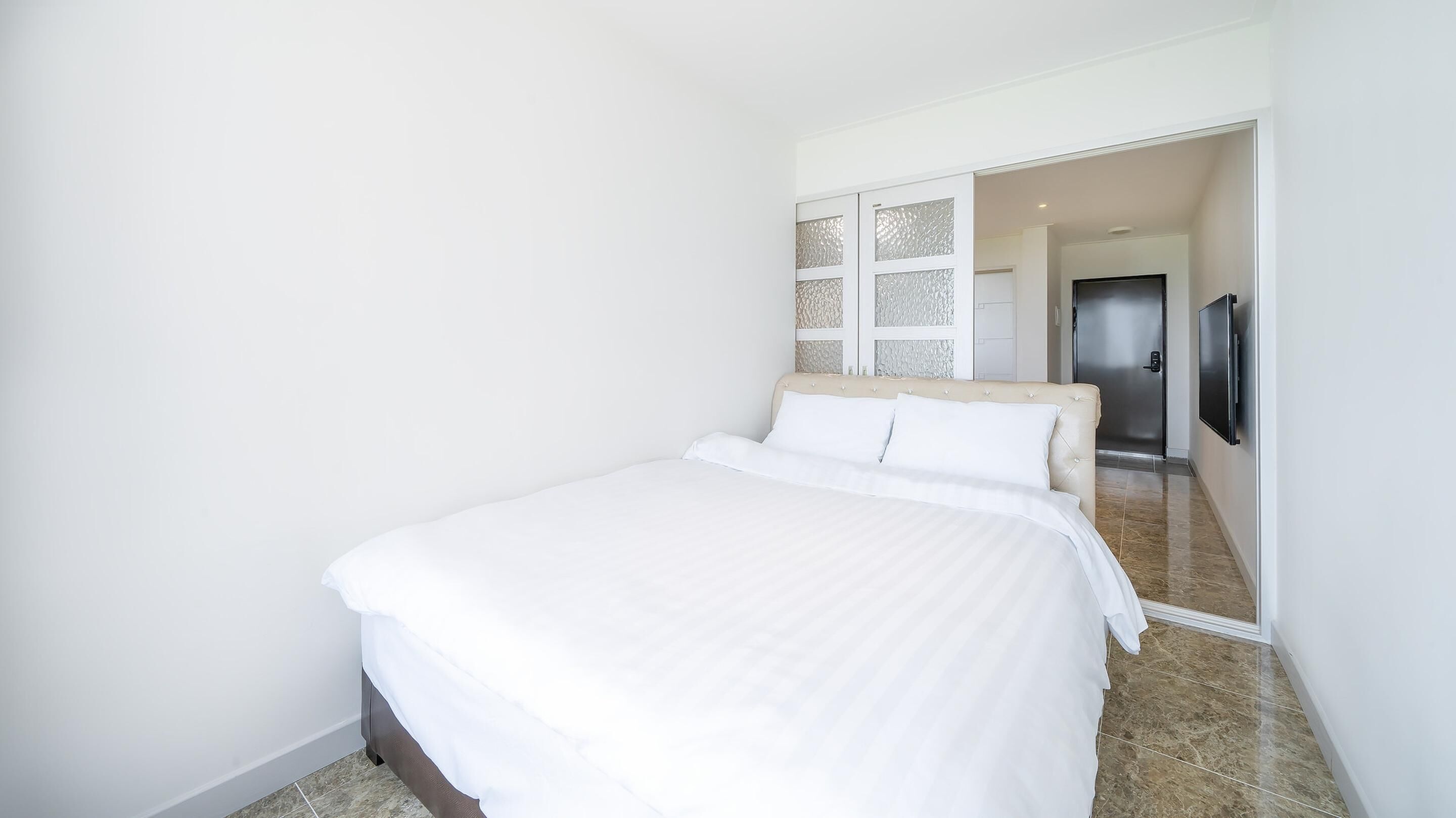 A bedroom with a bed, a television, and a door leading to another room.