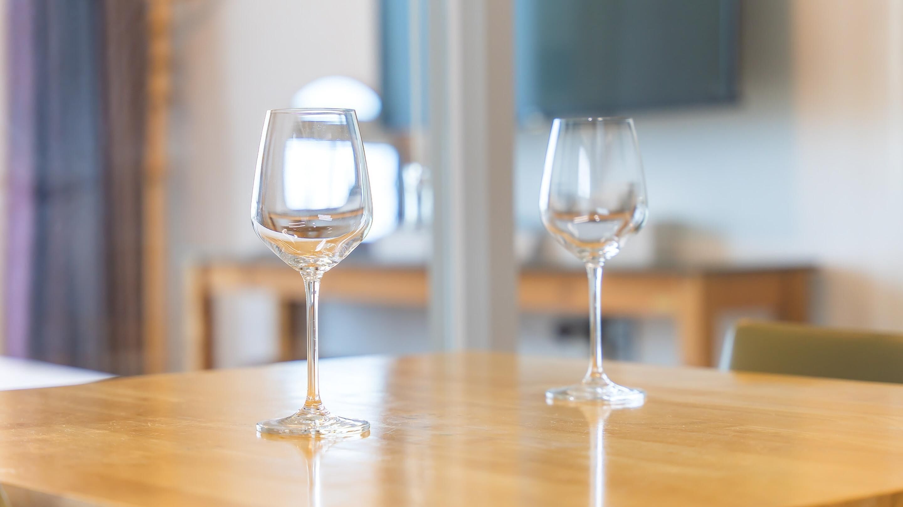 Deux verres à vin vides sont posés sur une table ronde en bois, dans une pièce dont le fond est flou.