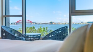 A room with a view of a red bridge over water, a cityscape, and wicker furniture. - Sokcho Ocean View Pension (Sokcho)
