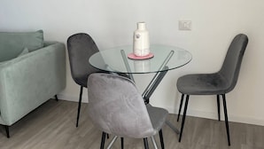 Moderni ruokailutila, jossa on lasipöytä, kaksi harmaata tuolia ja valkoinen maljakko, jonka pinnassa on musta kuvio.