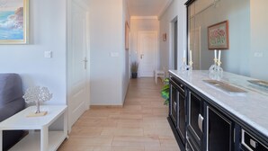 Un couloir avec un plancher en bois, un banc blanc, un meuble noir avec un miroir et un tableau accroché au mur.
