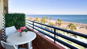 Un balcon avec une table et des chaises blanches, un pot de fleurs et une vue sur la plage et l’océan.
