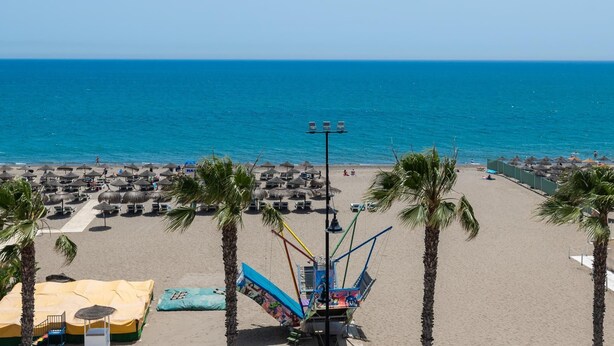 Une plage bordée de palmiers, avec des parasols et une structure colorée en forme de bateau.