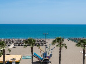 A beach with palm trees, umbrellas, and a colorful boat structure. - Apartamento Playa Los Álamos - Bajondillo, free parking (Torremolinos)