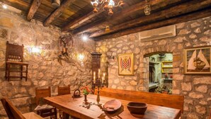 Une pièce rustique aux murs de pierre, avec une table à manger en bois, des bancs et un lustre.