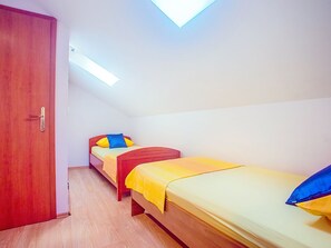 Une petite pièce, bien éclairée, avec deux lits, une porte en bois et un puits de lumière.