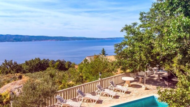 Un espace aménagé au bord de la piscine, avec des chaises longues et une table, donnant sur une étendue d’eau.
