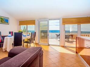 Un coin repas avec une table dressée pour deux personnes, un canapé et un balcon avec vue.