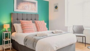 A neatly arranged bedroom with a bed, bedside table, lamp, and a chair.