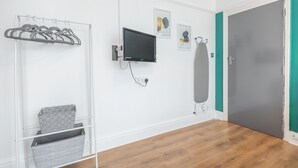 A room with a wooden floor, a grey door, a white wall with a mounted TV, a grey coat rack, and a grey storage unit.