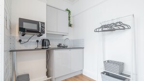 A compact kitchen with a microwave, kettle, and a small trash bin.