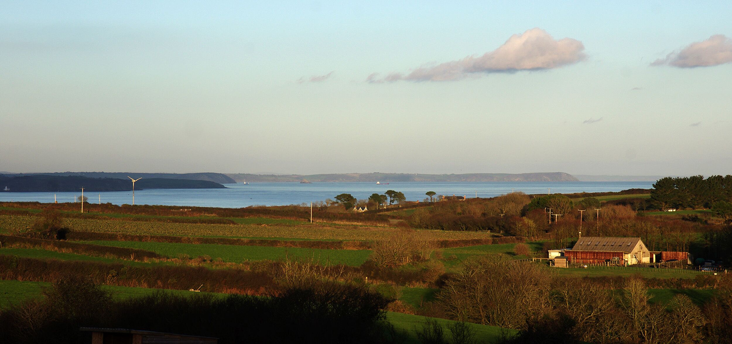 A rural landscape with fields, a body of water, and a small house with a sloped roof.