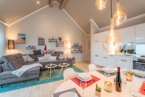 Een moderne woonkamer met een grijze bank, een eettafel voor twee personen en een keuken met witte kasten en een fornuis.