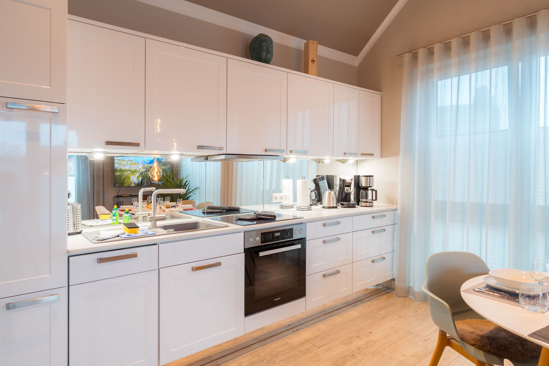 A modern kitchen with white cabinetry, a built-in oven, and a dining area with a table and chairs.