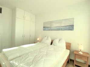 A bedroom with a bed, a nightstand, a lamp, a wardrobe, and a painting on the wall. - Hello and welcome to Apartment Fiete! (Dangast)