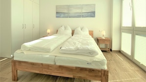 Une chambre à coucher avec un lit double, une table de chevet, une armoire et une grande fenêtre avec des stores.