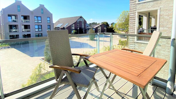 Un balcon avec des fauteuils en osier et une table en bois, donnant sur une cour intérieure bordée de bâtiments.