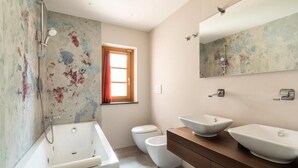 A bathroom with a bathtub, two sinks, a toilet, and a window with curtains. - Mathusalem   Deluxe Suite with Spa Bath (CORI)