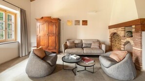 A living room with a wooden ceiling, a sofa set, two armchairs, a coffee table, and a stone fireplace. - Mathusalem   Deluxe Suite with Spa Bath (CORI)