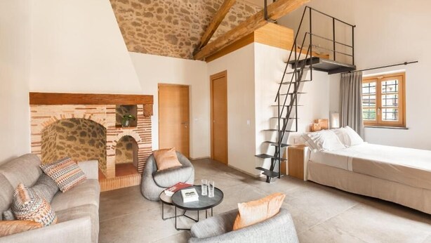 A spacious living room with a stone fireplace, a sofa, a coffee table, and a staircase. - Mathusalem   Deluxe Suite with Spa Bath (CORI)
