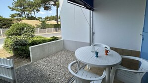 A balcony with a white table and chairs, a blue door, and a view of trees and a road. - Cozy 2-Room Apartment by the Beach with Terrace and Parking - Sleeps 4 (Saint-Jean-de-Monts)
