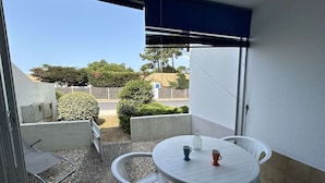 A balcony with a round table and chairs, a small potted plant, and a view of a residential area with trees and a fence. - Cozy 2-Room Apartment by the Beach with Terrace and Parking - Sleeps 4 (Saint-Jean-de-Monts)