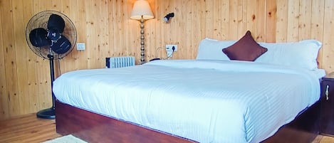 A wooden-paneled room with a bed, a standing fan, a lamp, and a white rug.