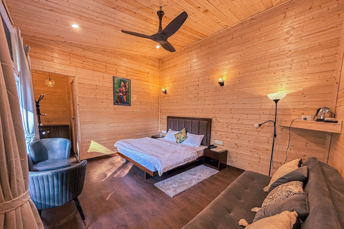 Un dormitorio con paneles de madera, una cama, una silla, un sofá, un ventilador de techo y una mesita de noche.