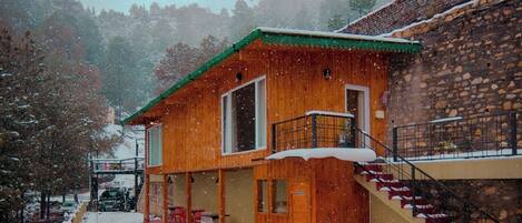 A wooden cabin with a green roof, a staircase, and a snow-covered ground.