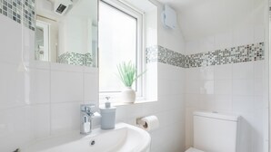 Un baño con lavamanos blanco, inodoro y ventana con planta.