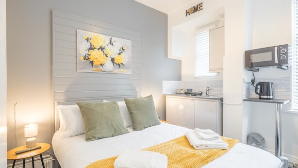 Habitación de hotel con cama, un cuadro, zona de cocina y un cartel que dice 'HOME'.