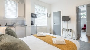 Habitación de hotel moderna con cama, mesita de noche, televisor y baño visible a través de una puerta abierta.