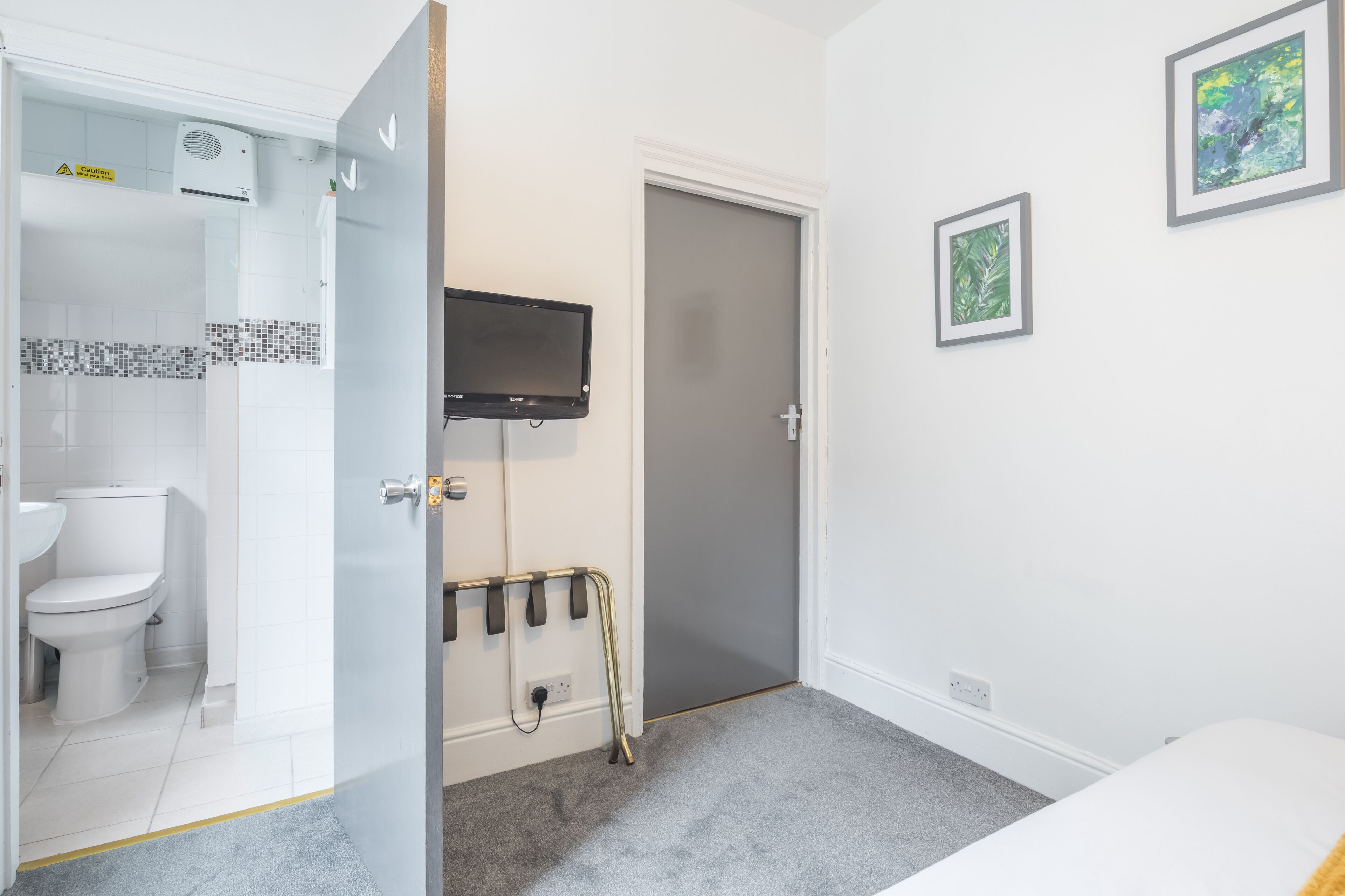 Et badeværelse med toilet, bruser og et ophængt TV.