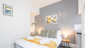 Un dormitorio ordenado con cama, mesita de noche y una obra de arte colgada en la pared.