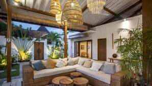 A cozy, well-lit living area with wicker furniture, wooden accents, and lush greenery.