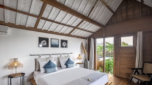 A spacious bedroom with a large bed, wooden beams, a view of the outdoors, and a chair by the window.
