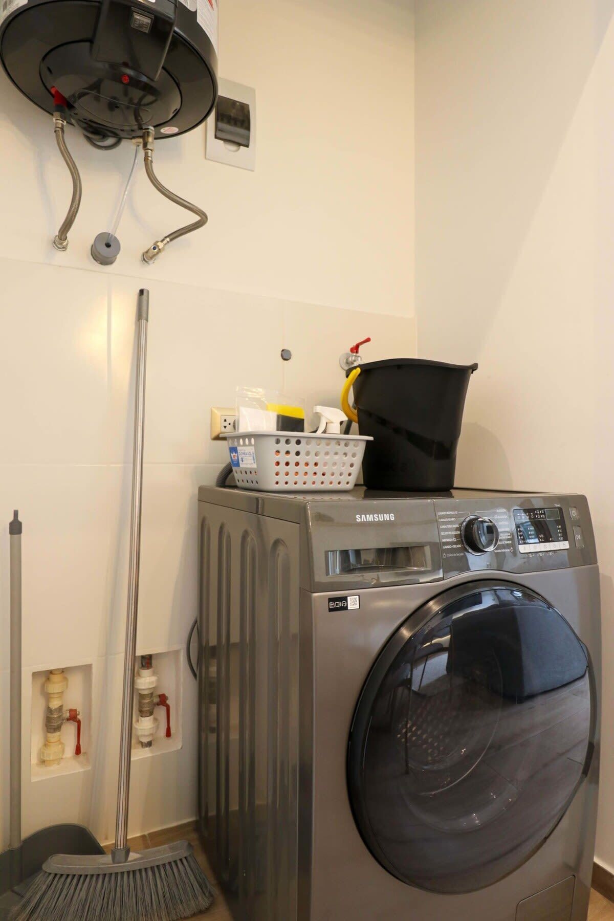 A compact laundry room with a Samsung washing machine, a dryer, and a broom.