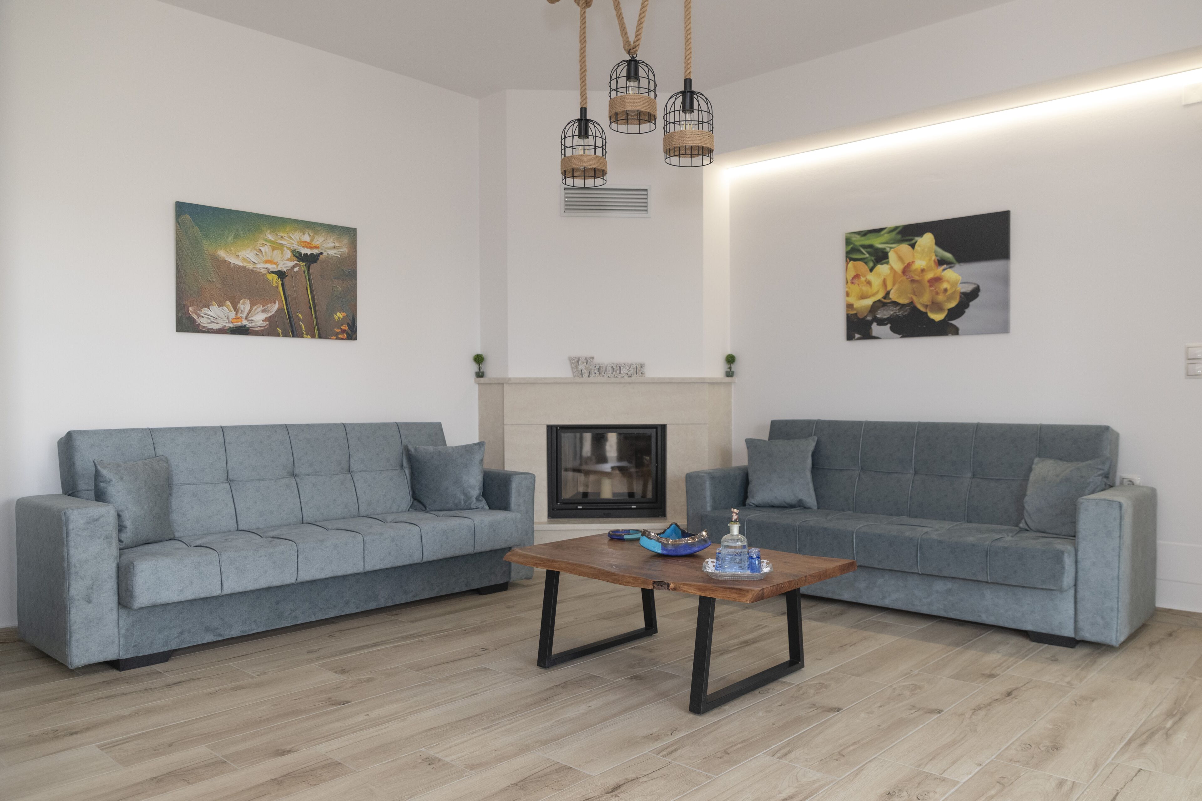 Uma sala de estar moderna com dois sofás cinza, uma mesa de centro de madeira e duas pinturas penduradas na parede.
