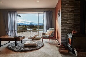 A modern living room with a large sliding glass door leading to a scenic outdoor view, a fireplace, and comfortable seating. - Mountain View Abode - Spectacular Views In Twizel (Twizel)