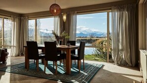 Ein Essbereich mit Tisch und Stühlen, großen Fenstern mit Vorhängen und Blick auf Berge und See.