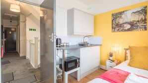 A compact hotel room with a kitchenette, a bed with a yellow pillow, and a painting on the wall. - The Modern Cambridge Studio 3 (Cambridge)