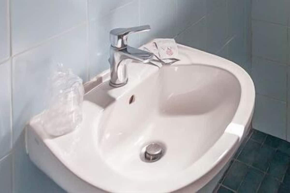 A white bathroom sink with a silver faucet, a soap dispenser, and a drain.