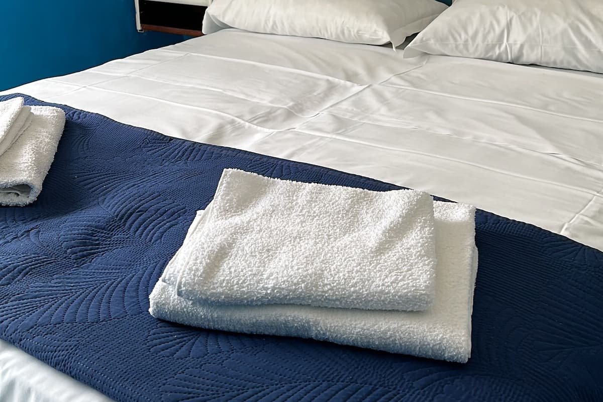 A hotel room with a bed, a nightstand, a wall-mounted light, and a sign above the bed.