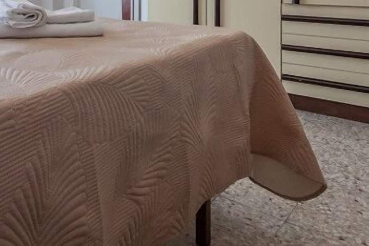 A neatly made bed with a beige bedspread and white linens.